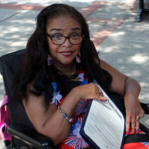 A woman in a wheelchair holds a document, appearing attentive and ready to discuss its contents.