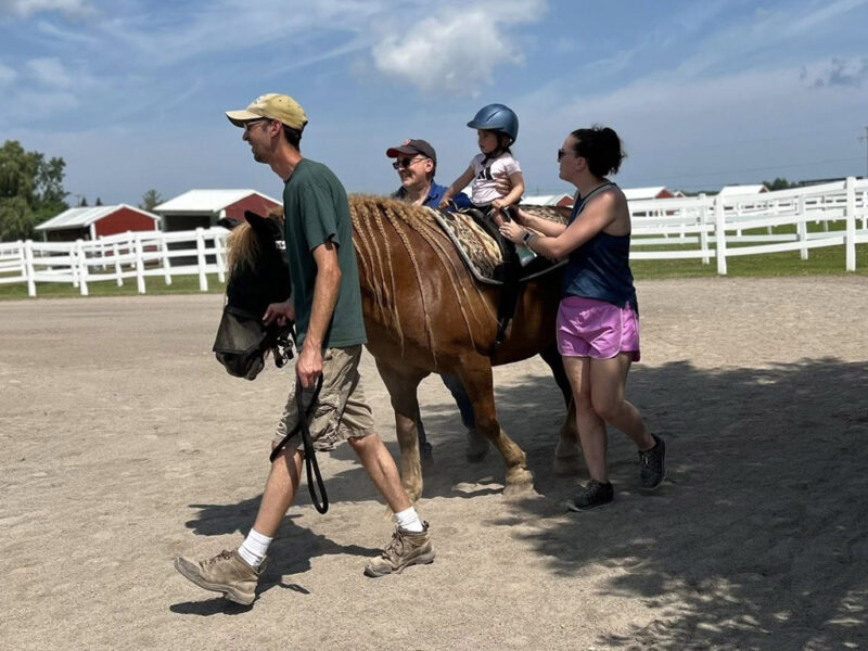 child-riding-a-horse-with-adults child riding a horse with adults on his side